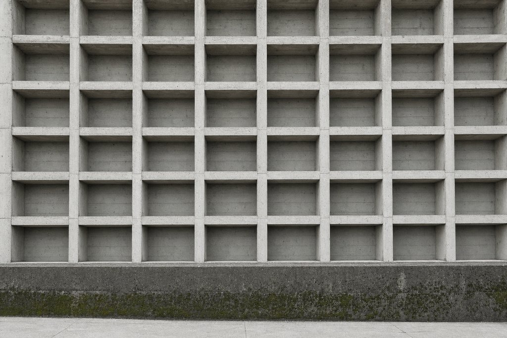 A concrete wall of empty rectangular archive niches receding across the frame.