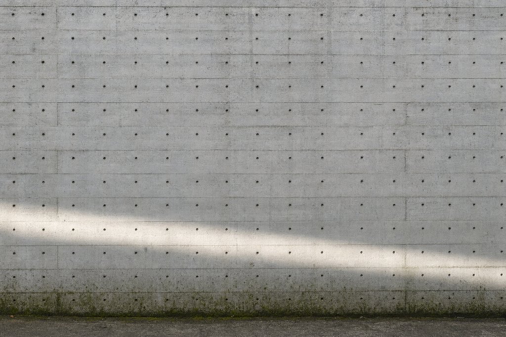 A blank concrete wall in raking light, marked by the grid of holes left by removed formwork ties.